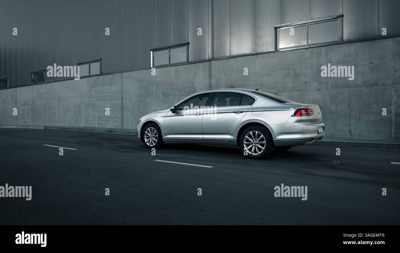 Silver Volkswagen Passat garé près de l'entrepôt. Vue latérale de la berline allemande près du mur de béton gris. Banque D'Images