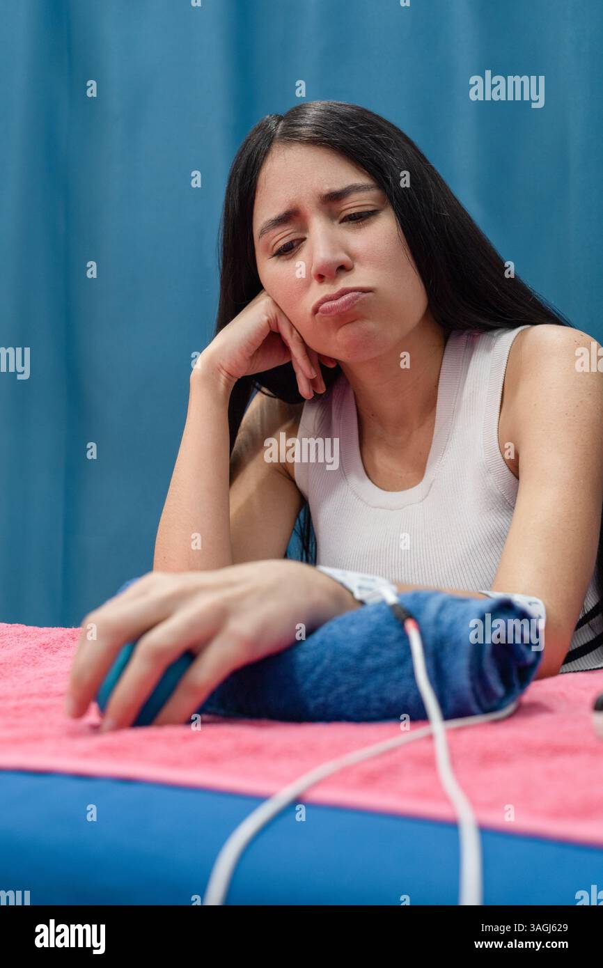 Jeune femme avec une expression fatiguée recevant une électrothérapie de bras tout en posant son bras sur une serviette pendant le traitement. Banque D'Images