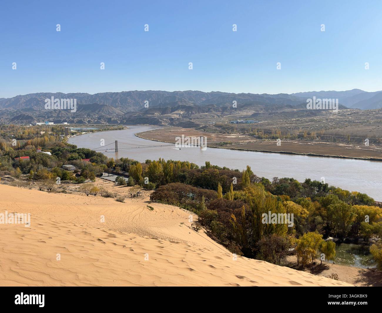 Rivière jaune qui coule à travers un paysage, encadrée par des montagnes et des dunes de sable majestueuses. Banque D'Images