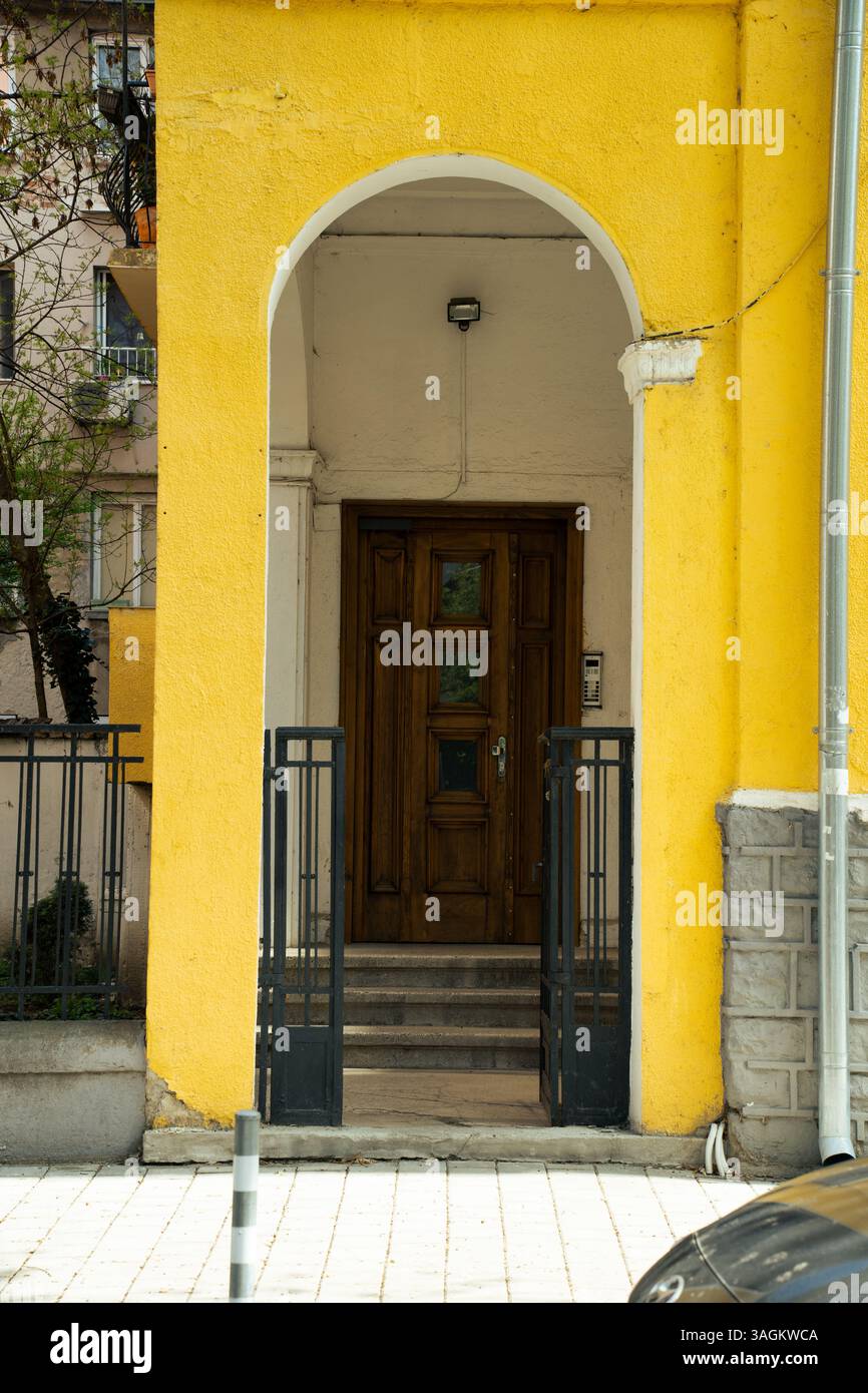 Entrée voûtée d'un immeuble résidentiel avec une porte en bois encadrée par une façade jaune vif et portail en métal noir. Banque D'Images