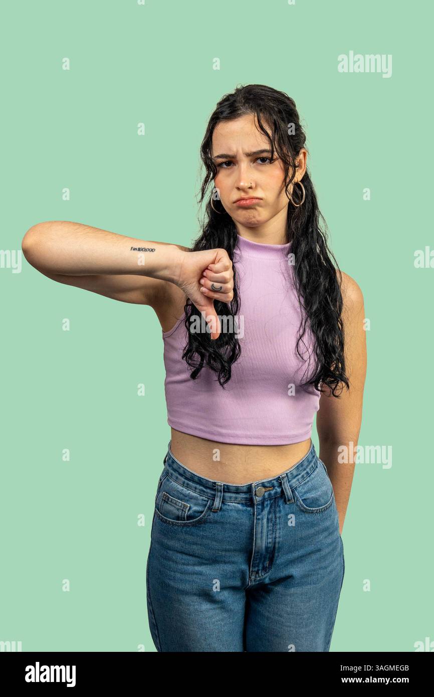 Jeune femme montrant le pouce vers le bas geste, exprimant la désapprobation et la rétroaction négative sur un fond vert Banque D'Images