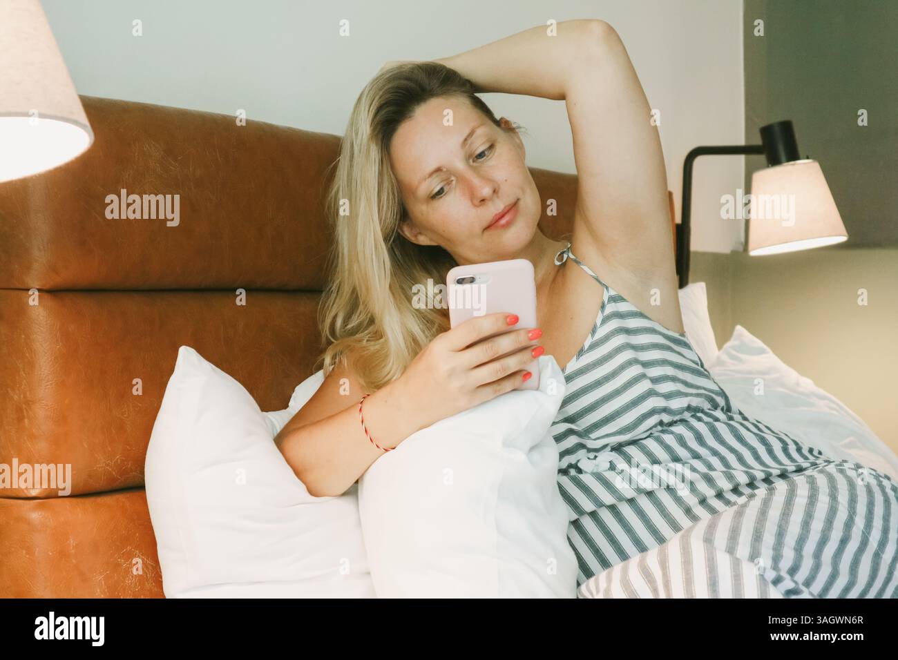 Belle femme blonde à l'aide d'un smartphone couché sur le lit dans la chambre Banque D'Images