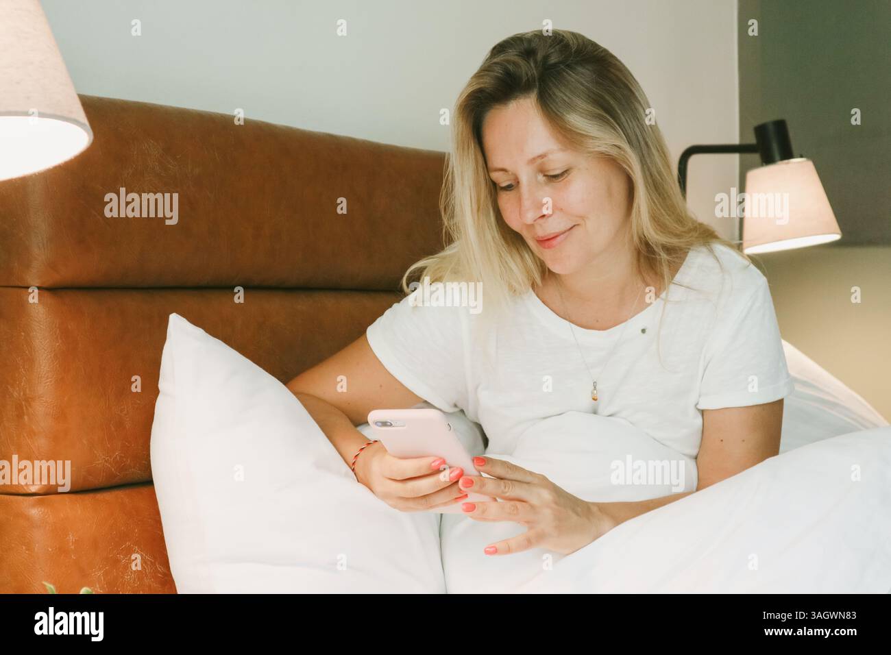 Belle femme blonde à l'aide d'un smartphone couché sur le lit dans la chambre Banque D'Images