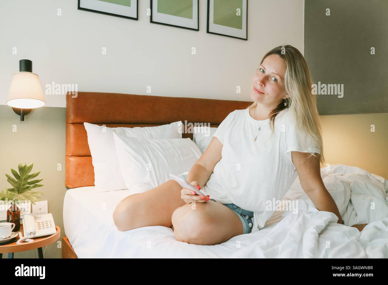 Belle femme blonde à l'aide d'un smartphone couché sur le lit dans la chambre Banque D'Images