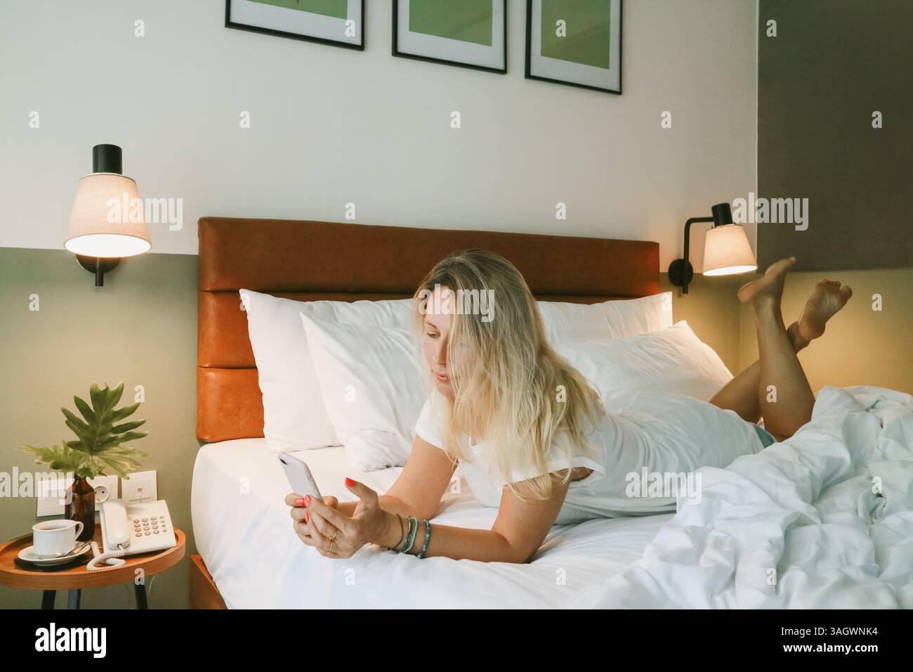 Belle femme blonde à l'aide d'un smartphone couché sur le lit dans la chambre Banque D'Images