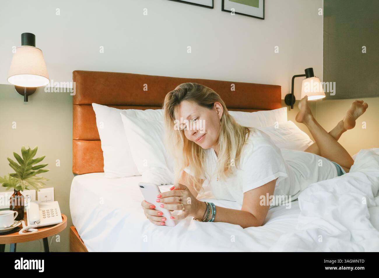 Belle femme blonde à l'aide d'un smartphone couché sur le lit dans la chambre Banque D'Images
