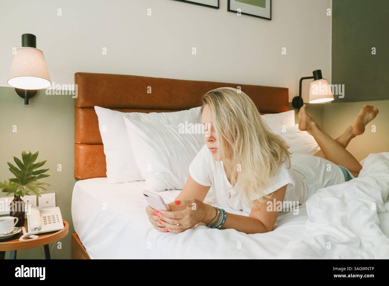 Belle femme blonde à l'aide d'un smartphone couché sur le lit dans la chambre Banque D'Images