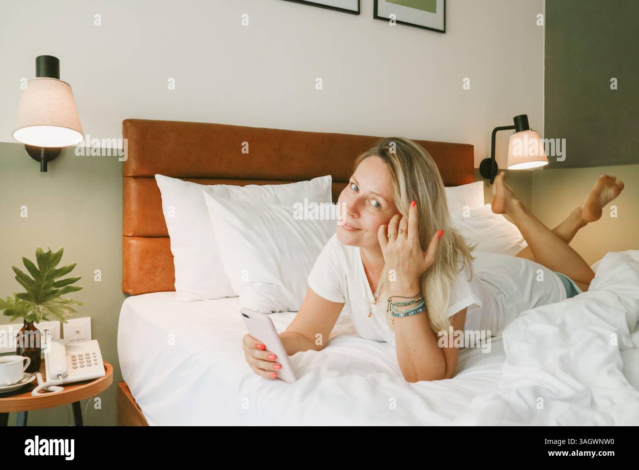 Belle femme blonde à l'aide d'un smartphone couché sur le lit dans la chambre Banque D'Images