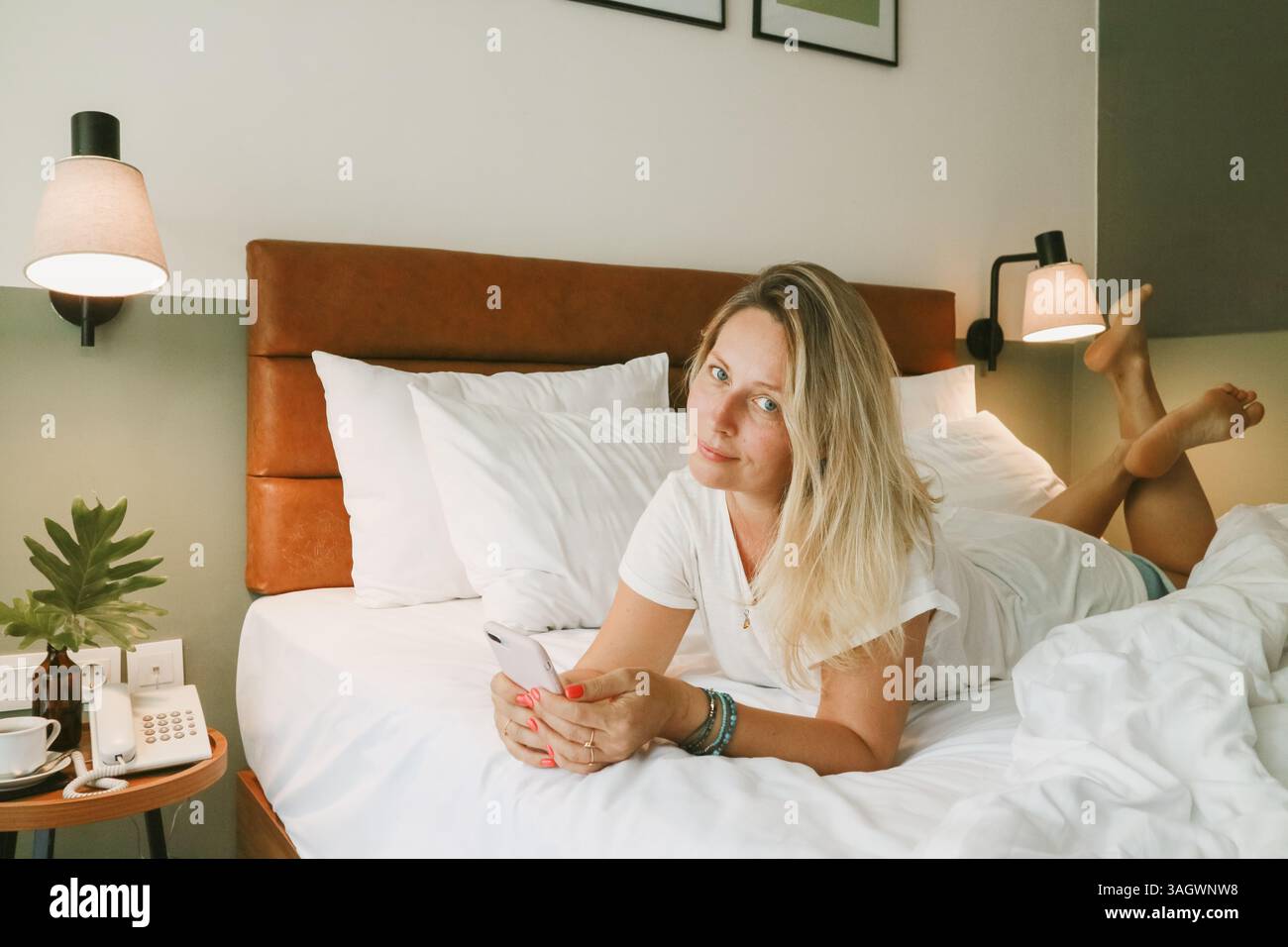 Belle femme blonde à l'aide d'un smartphone couché sur le lit dans la chambre Banque D'Images