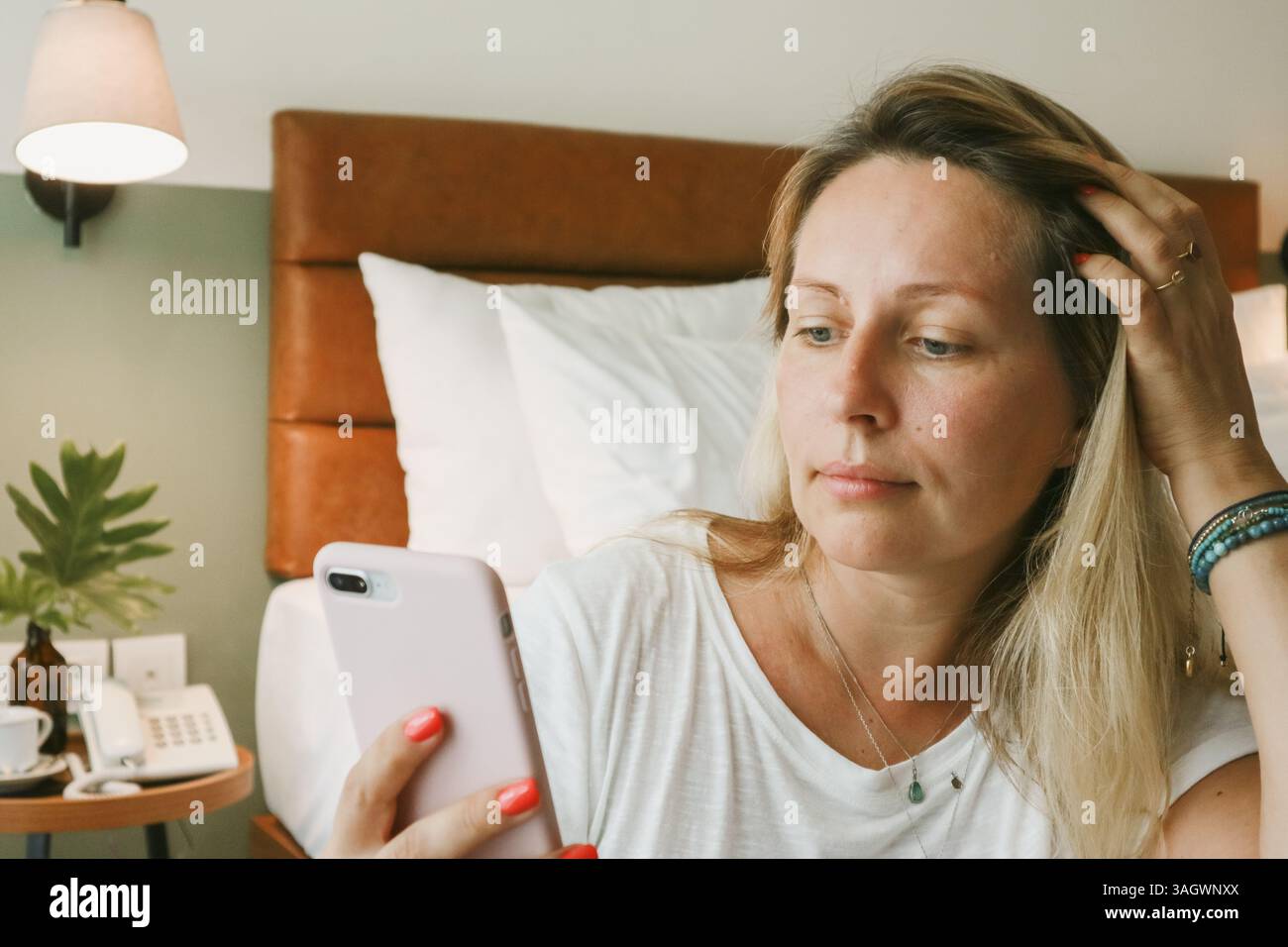 Belle femme blonde à l'aide d'un smartphone couché sur le lit dans la chambre Banque D'Images