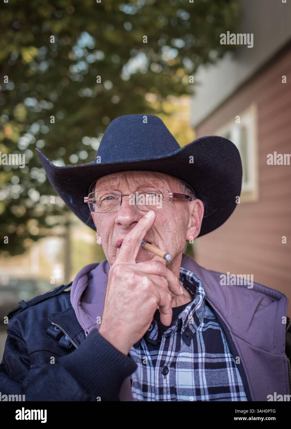 Fermier avec chapeau fumant cigarette. Portrait d'un vieil homme âgé fumant un cigare. Homme portant un chapeau de cow-boy fumant un cigarillo. Cow-boy fumant un cigare Banque D'Images