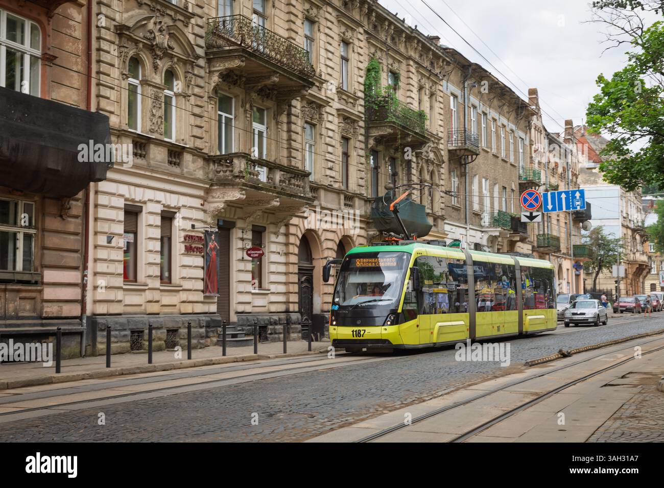 LVIV, UKRAINE - 20 juin 2021 : un tramway animé parcourt une rue pavée entourée de bâtiments historiques. La ville respire le charme avec une architecture ornée et une atmosphère animée par une journée nuageuse. Banque D'Images