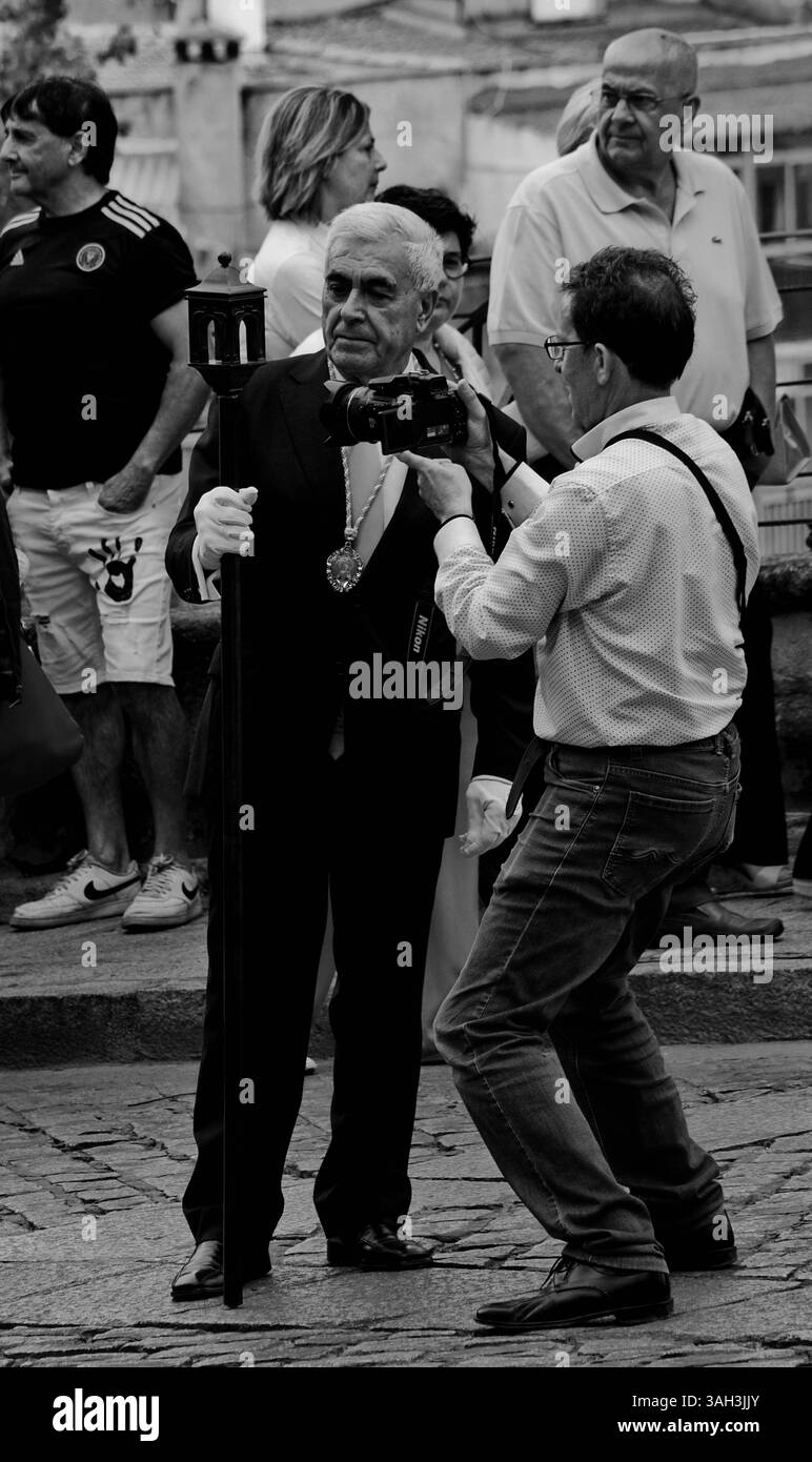 Un groupe de personnes s'est rassemblé à l'extérieur, avec une personne tenant un bâton et portant un médaillon. Une autre personne prend une photo de cette personne Banque D'Images