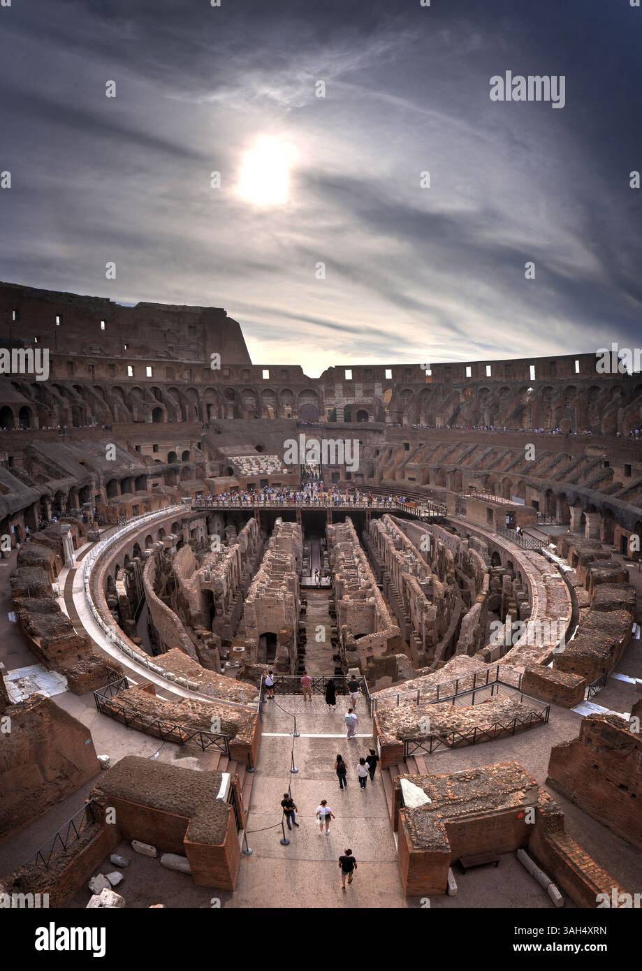 Vue panoramique verticale grand angle du Colisée à Rome, Italie vue face à l'est avec le soleil levant dans un ciel matinal dramatique avec des touristes. Banque D'Images Vue panoramique verticale grand angle du Colisée à Rome, Italie vue face à l'est avec le soleil levant dans un ciel matinal dramatique avec des touristes. Banque D'Images