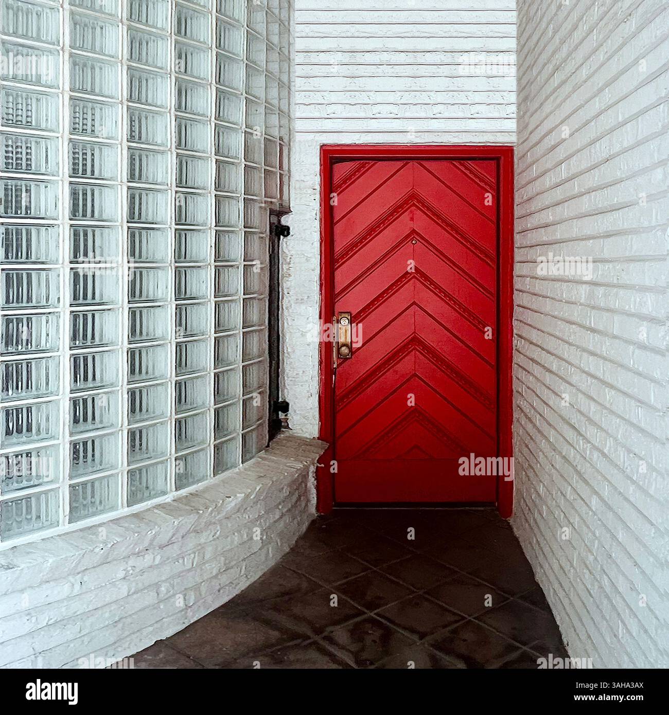 Porte rouge de style Art moderne frappante encadrée par des blocs de verre incurvés et des murs de briques blanches, créant une entrée audacieuse et profilée à Chicago Banque D'Images