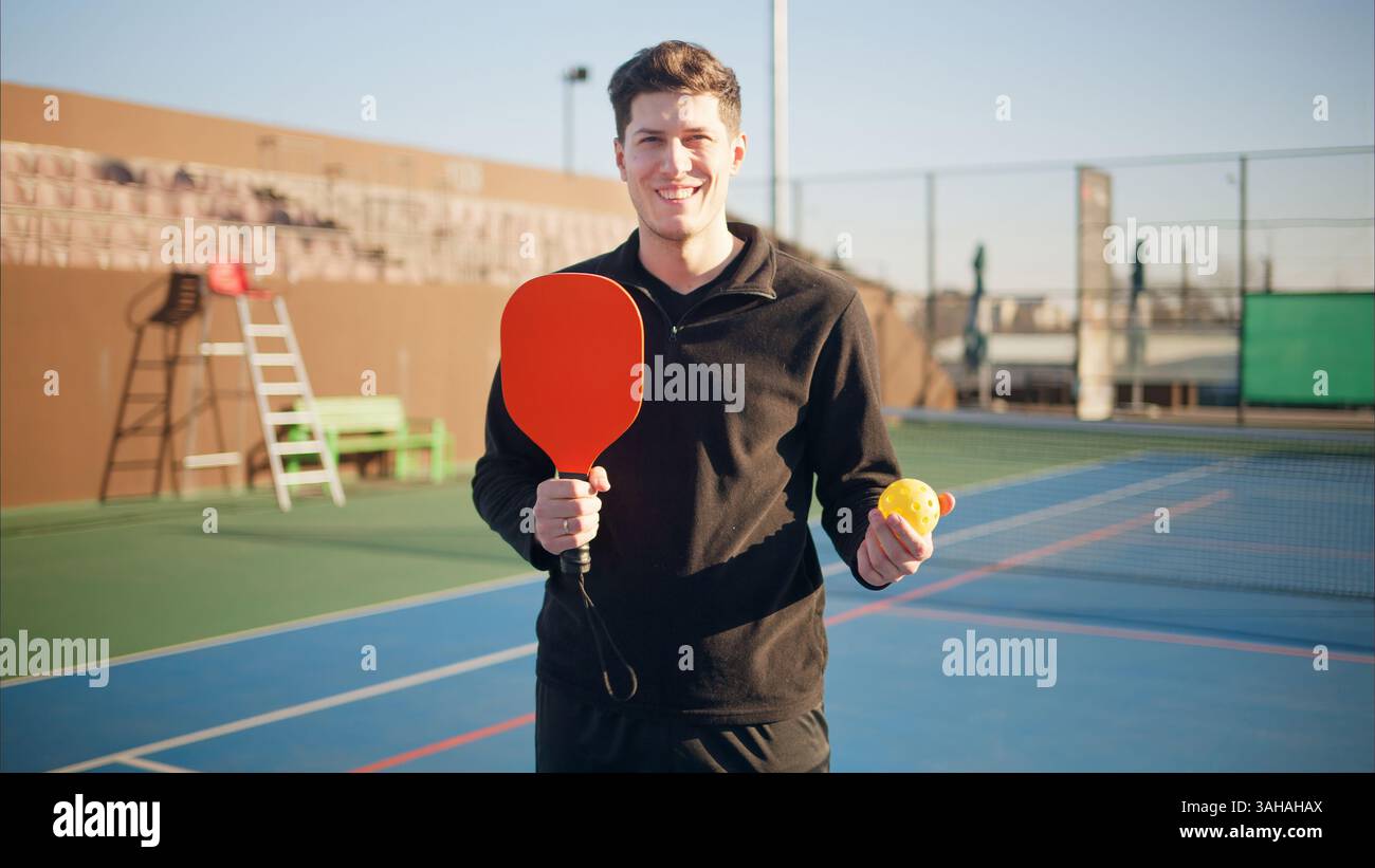 Portrait d'un jeune homme heureux et souriant tenant une pagaie de pickleball et un ballon sur un terrain Banque D'Images
