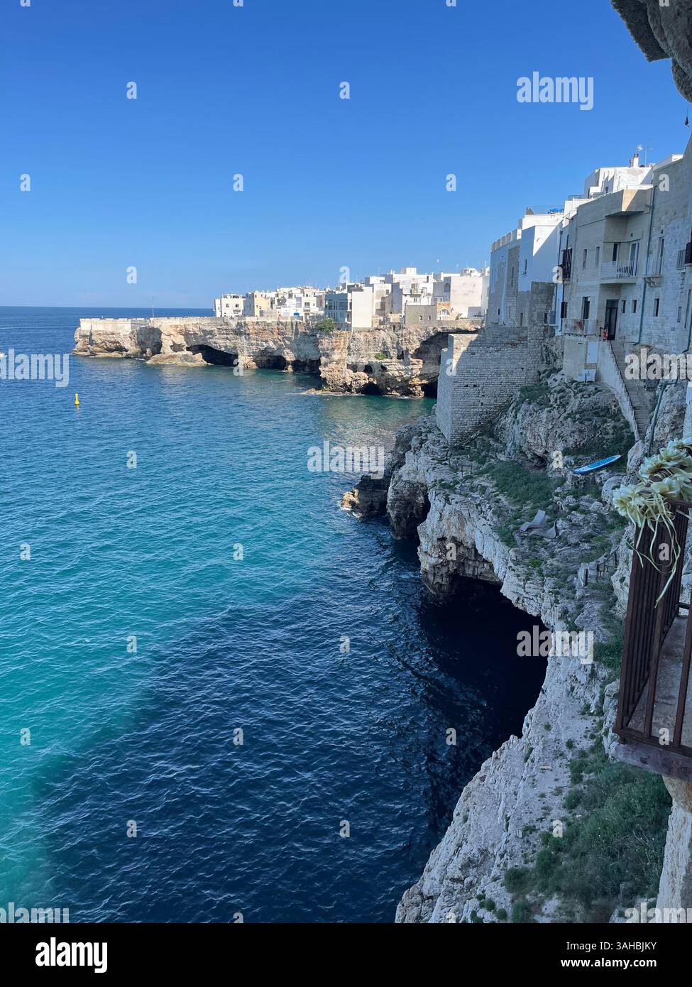 Vue sur la falaise de Polignano a Mare en Italie, avec des bâtiments blancs au-dessus des eaux turquoises. Une ville côtière méditerranéenne classique parfaite pour voyager. - Image de stock capturée avec un smartphone