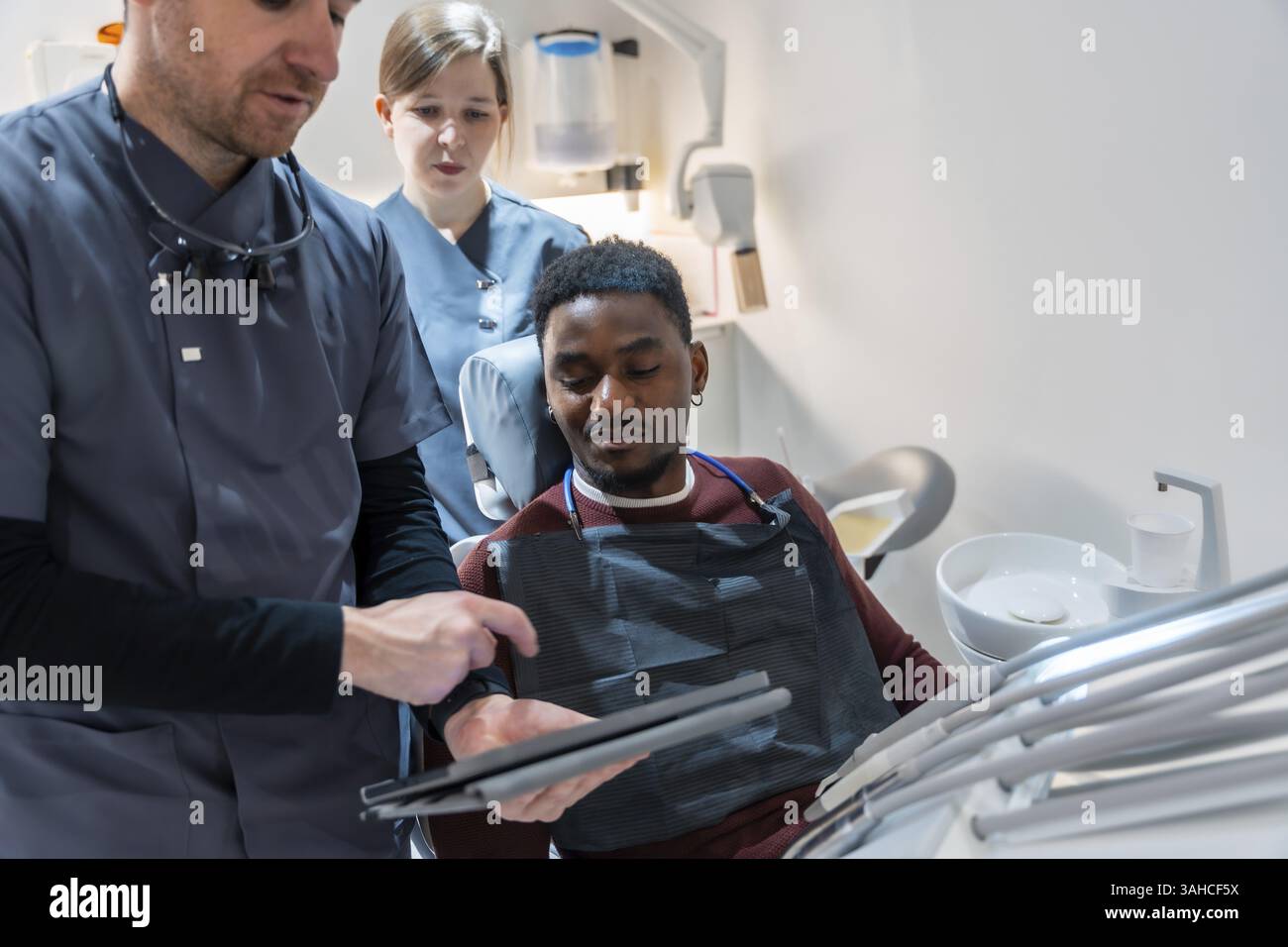 Dentiste et infirmière montrant les résultats de scintigraphie dentaire sur tablette numérique au patient dans la clinique moderne Banque D'Images