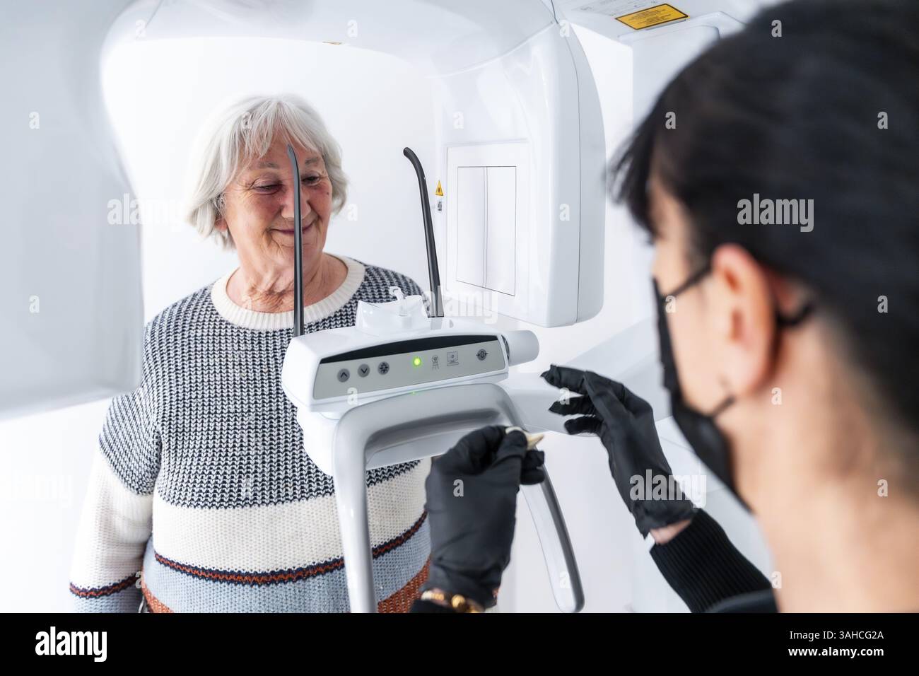 Dentiste exploitant une machine à rayons X, préparant un scanner dentaire pour une patiente âgée dans une clinique dentaire moderne Banque D'Images Dentiste exploitant une machine à rayons X, préparant un scanner dentaire pour une patiente âgée dans une clinique dentaire moderne Banque D'Images