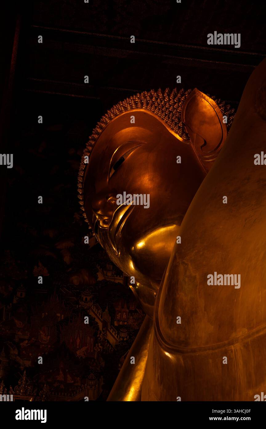 Visage du Bouddha couché à Wat Pho, avec des peintures murales du temple légèrement brillantes en arrière-plan Banque D'Images