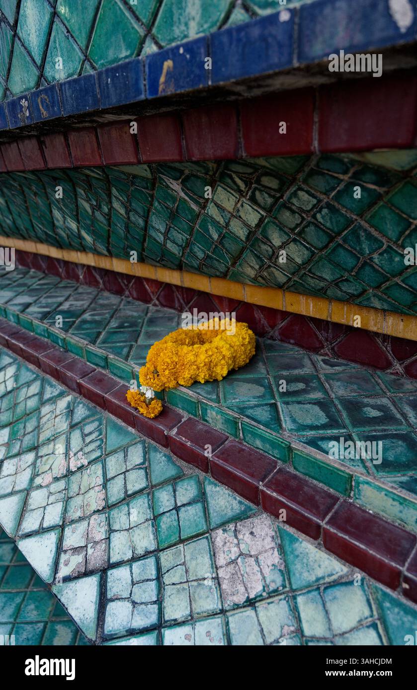 Une offrande de soucis repose doucement sur les tuiles de temple portées par le temps brillantes sur une toile de verts et de bleus délavés Banque D'Images