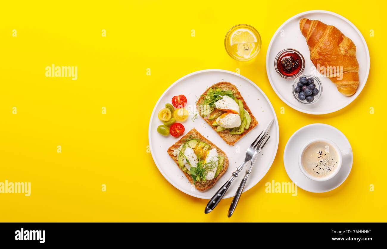 Petit déjeuner avec de délicieux toasts à l'avocat garni d'œufs pochés parfaitement cuits et croissant croustillant avec des baies et de la confiture Banque D'Images