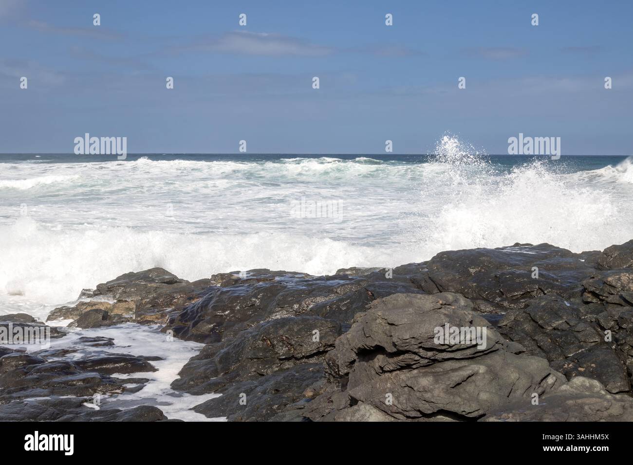 Grosses roches noires volcaniques sur la côte de l'océan Atlantique avec des vagues intenses pendant la journée venteuse d'hiver. Ciel bleu avec des nuages blancs. Las Palmas, Gran Canar Banque D'Images
