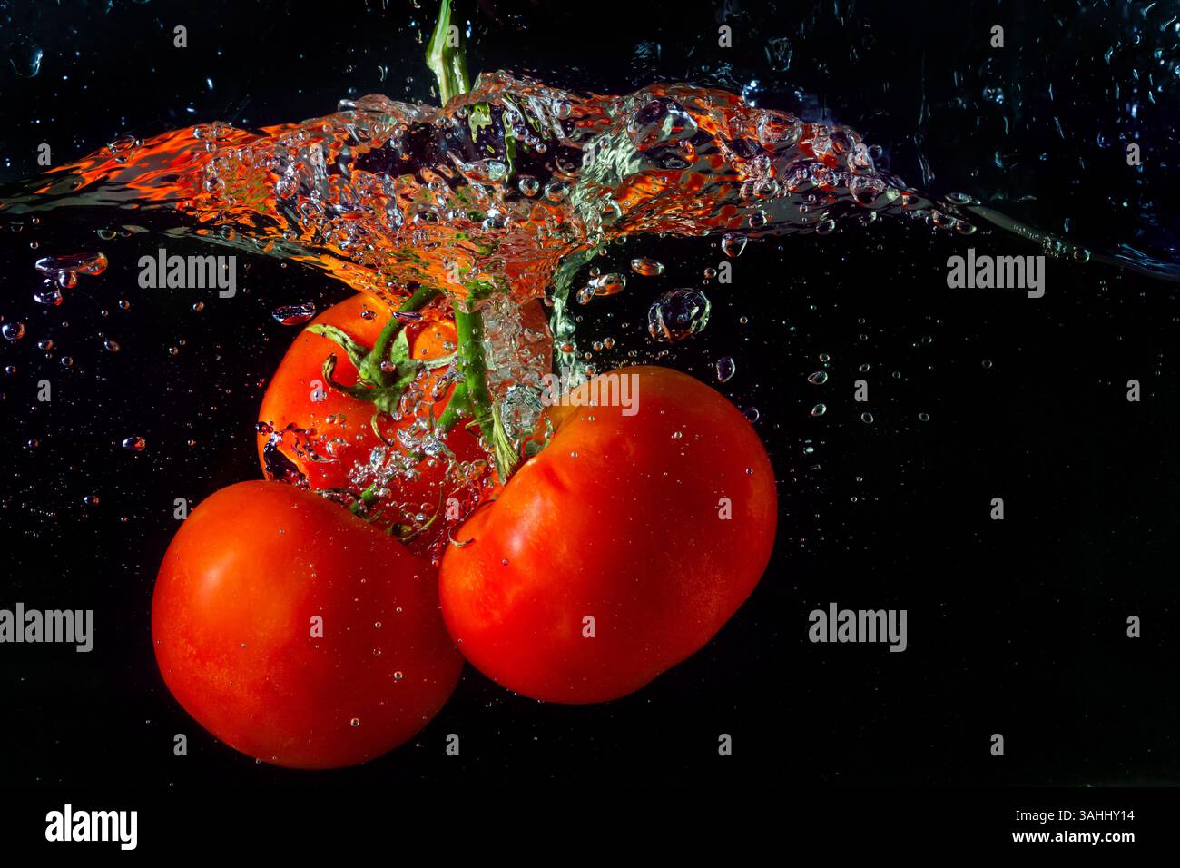 Tomate rouge fraîche tombant dans l'eau avec des éclaboussures d'eau et des bulles d'air isolées sur fond noir. Banque D'Images