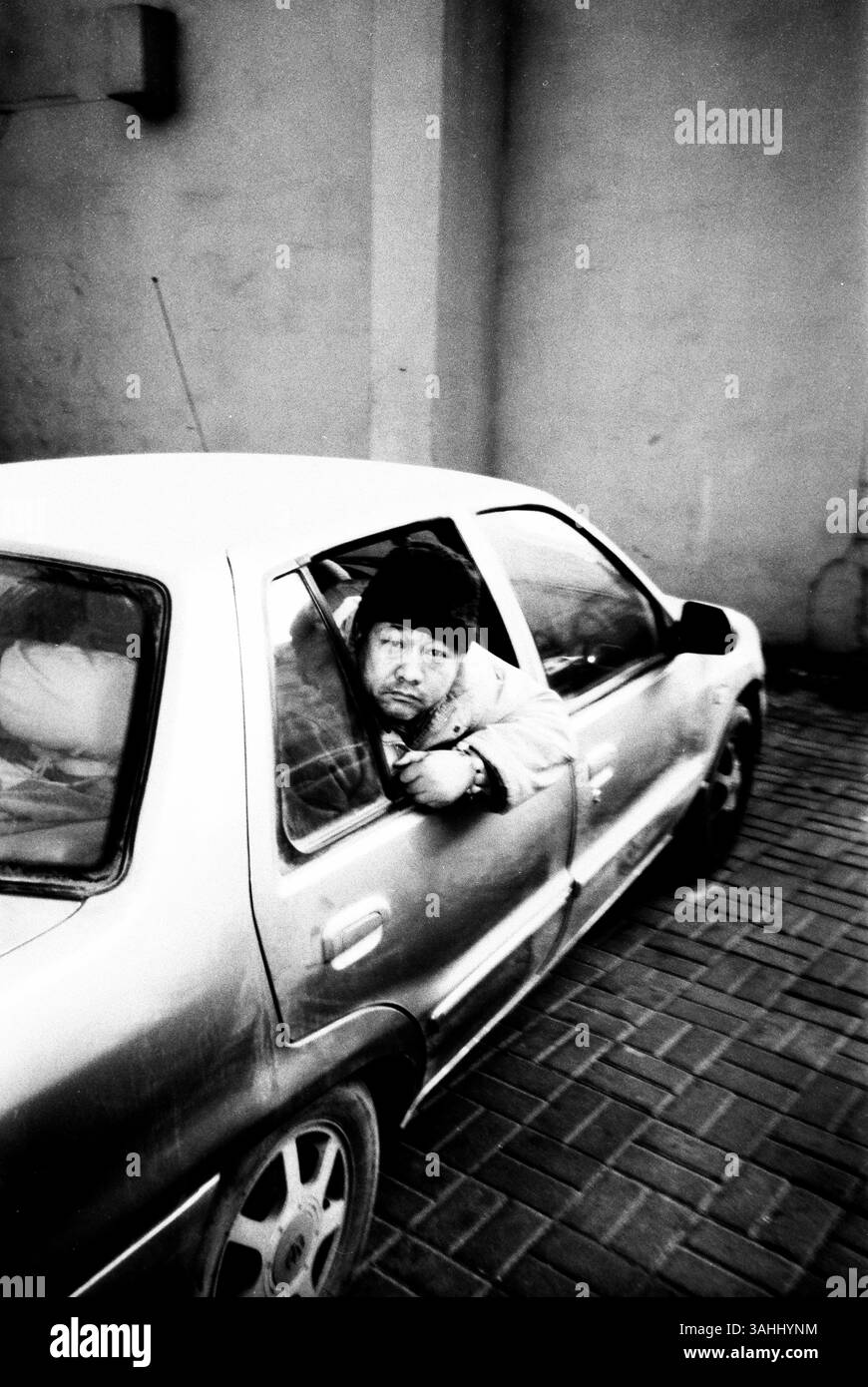 Homme penché par la fenêtre de la voiture – 2012 photographie de rue à Tianjin, Chine capturant l'isolement urbain et le réalisme Banque D'Images