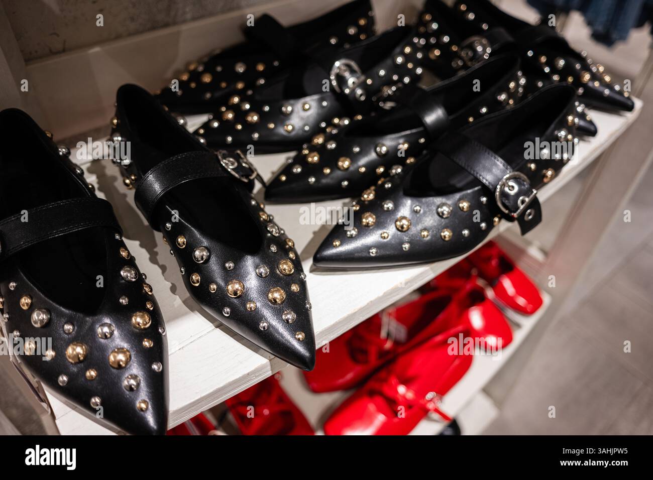 Élégantes chaussures plates en cuir noir ornées de clous associées à des chaussures rouges dans un présentoir de magasin. Banque D'Images