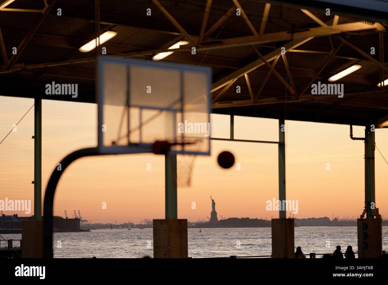 Silhouette de basket-ball et de ballon contre un coucher de soleil avec la Statue de la liberté au loin. New York, États-Unis Banque D'Images