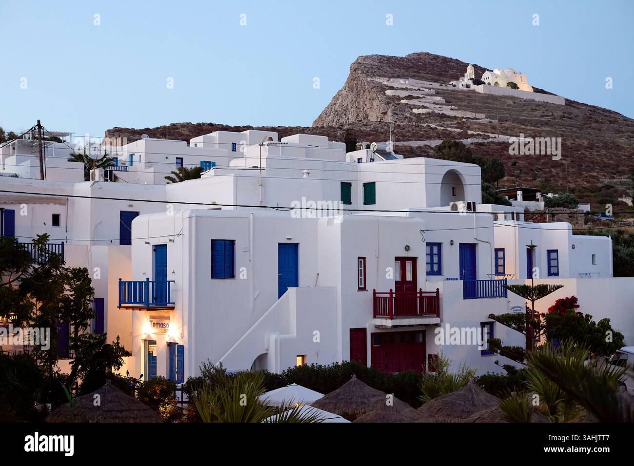 Bâtiments blancs avec volets bleus sous une colline rocheuse avec une petite église au loin. Banque D'Images