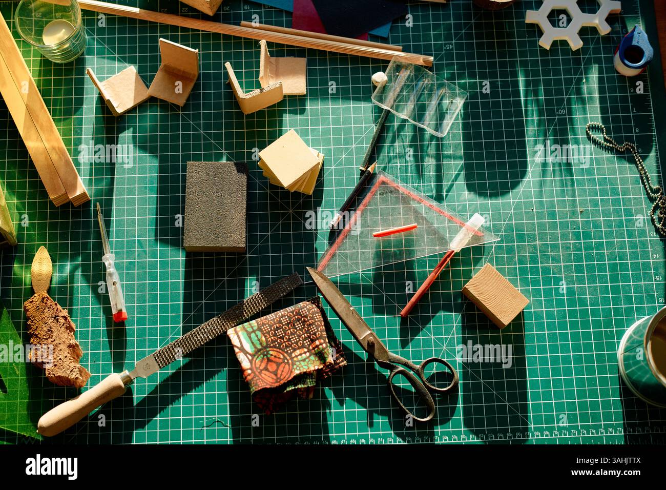 Fournitures d'art et outils disposés sur un tapis de découpe vert, éclairé par la lumière chaude du soleil. Banque D'Images