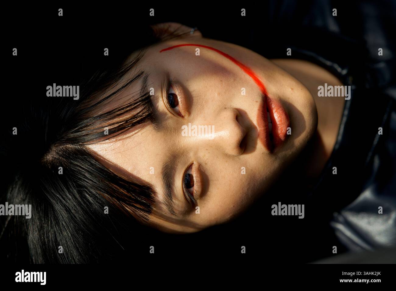 Gros plan d'une personne avec une ligne de peinture rouge sur son visage, dans un éclairage dramatique. Brandebourg, Allemagne Banque D'Images