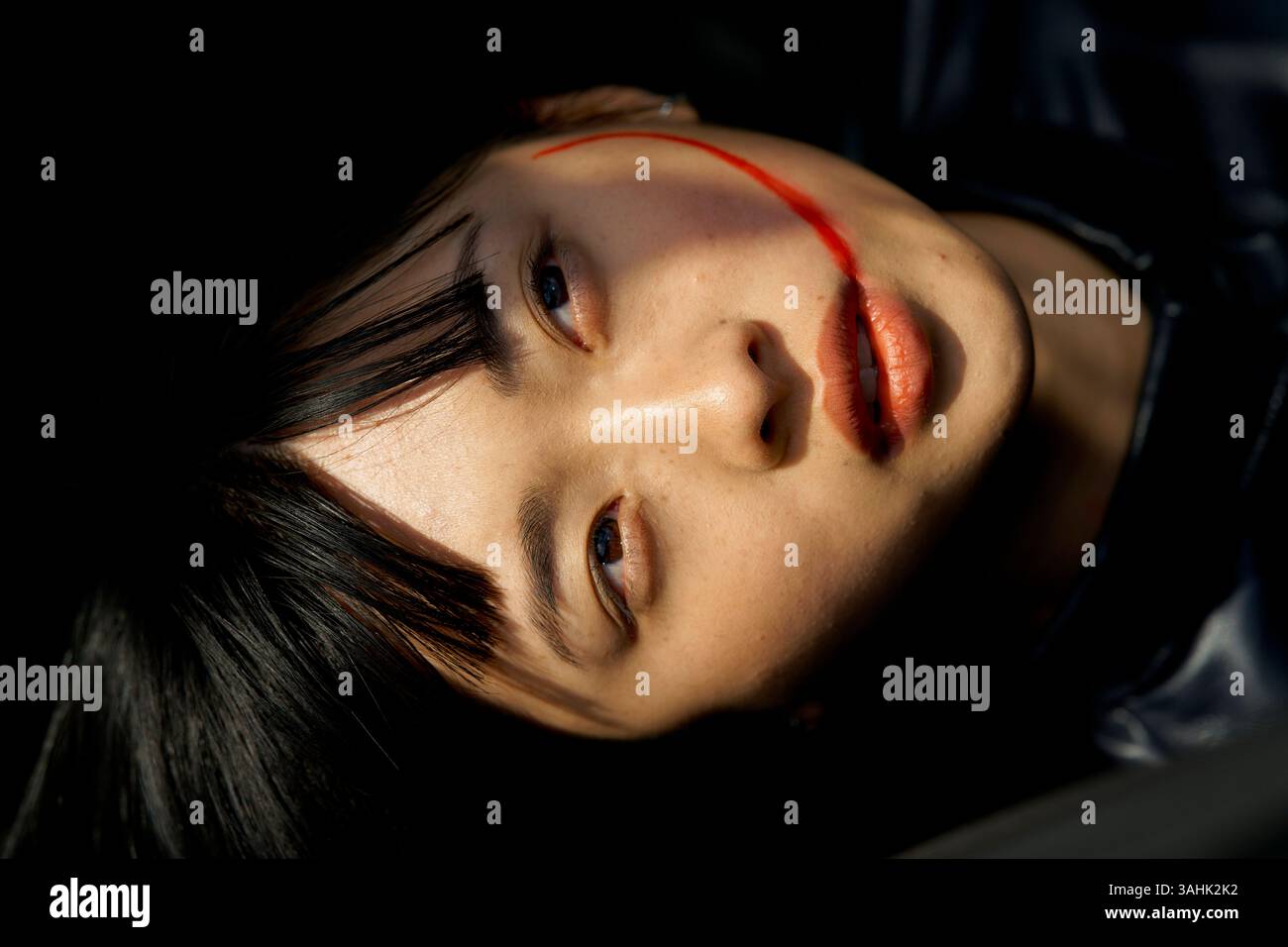 Femme allongée avec une traînée rouge sur son visage, portant une tenue sombre. Brandebourg, Allemagne Banque D'Images