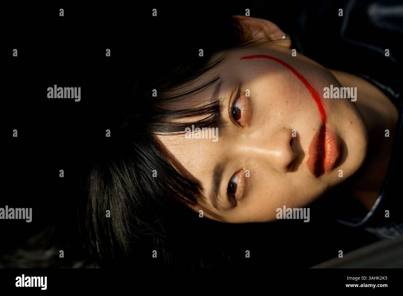 Une femme aux cheveux foncés et à la peinture rouge du visage sur ses joues regarde vers le haut sur un fond sombre. Brandebourg, Allemagne Banque D'Images
