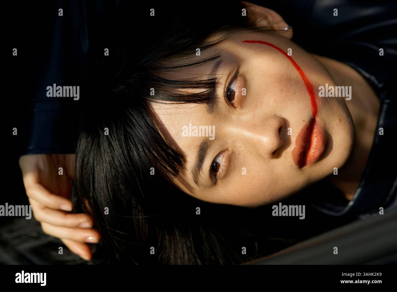 Femme avec une ligne de maquillage rouge à travers le visage couché avec l'expression contemplative Brandenburg, Allemagne Banque D'Images