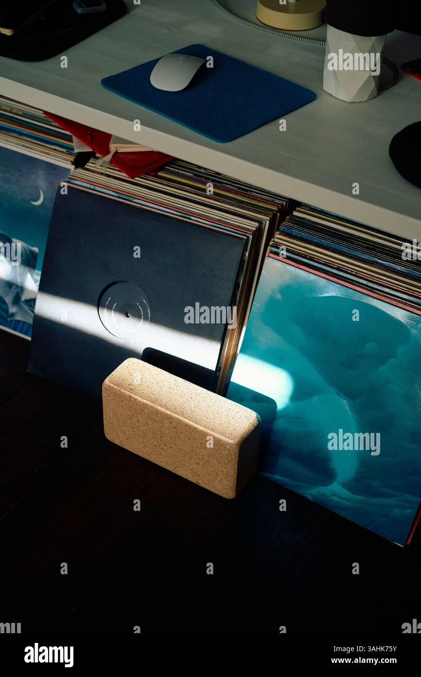 Disques vinyles empilés sous une étagère avec un ordinateur et une souris, frappés par un rayon de soleil. Banque D'Images