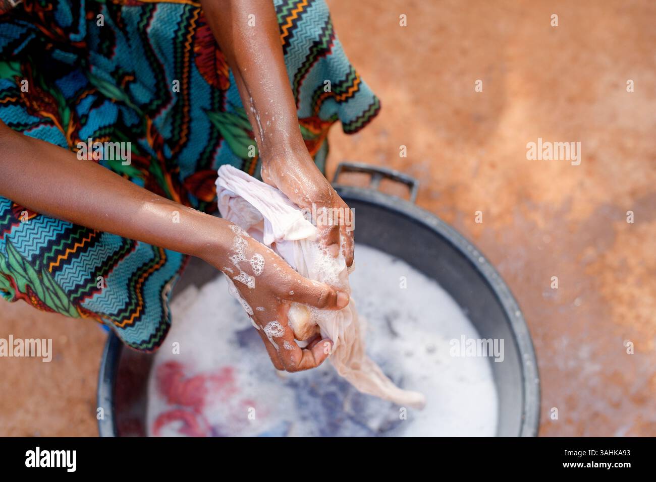 Mains lavant les vêtements dans l'eau savonneuse, portant un tissu coloré à motifs, à l'extérieur. Tanzanie, Afrique Banque D'Images