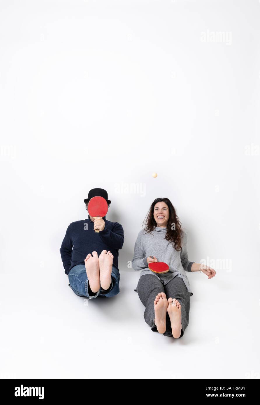 Une femme et un homme jouent au tennis de table. Leurs jambes sont écartées, l'homme a sa pagaie couvrant son visage, la fille rit en jouant. sce isolé Banque D'Images