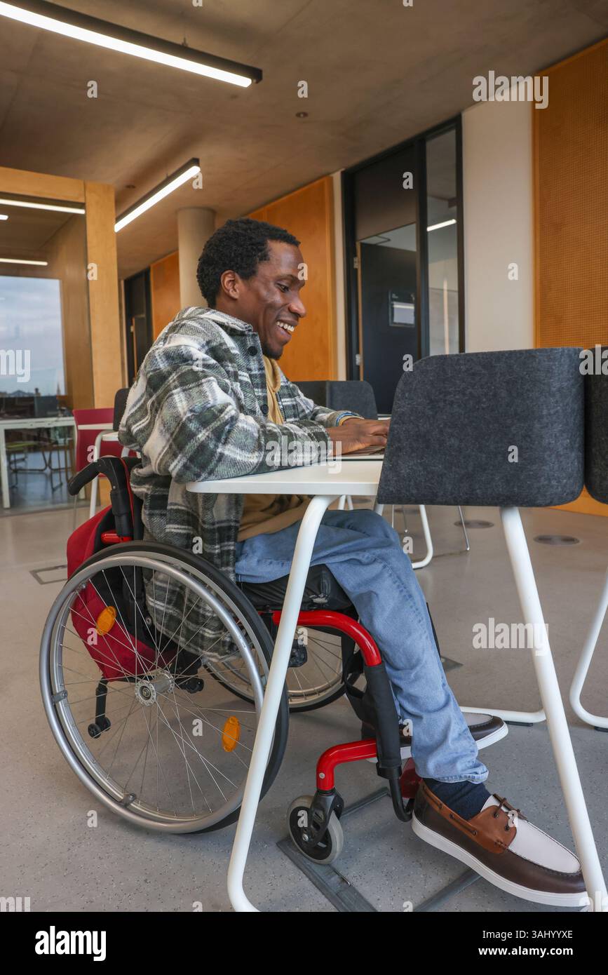 Homme en fauteuil roulant utilisant un ordinateur portable au bureau Banque D'Images