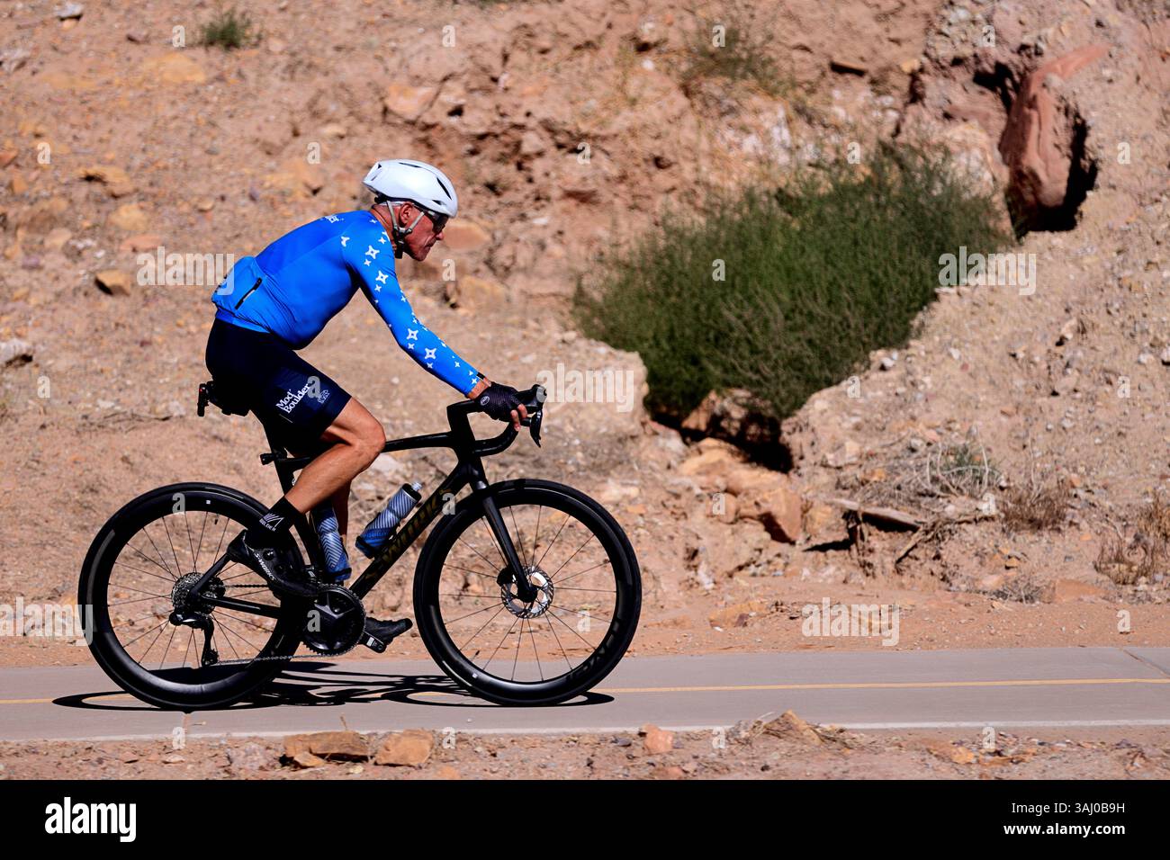 Un cycliste portant un maillot bleu Björka roule sur un vélo de route Trek noir sur une route pavée à travers le terrain accidenté de Moab, Utah, entouré de paysages rocheux Banque D'Images