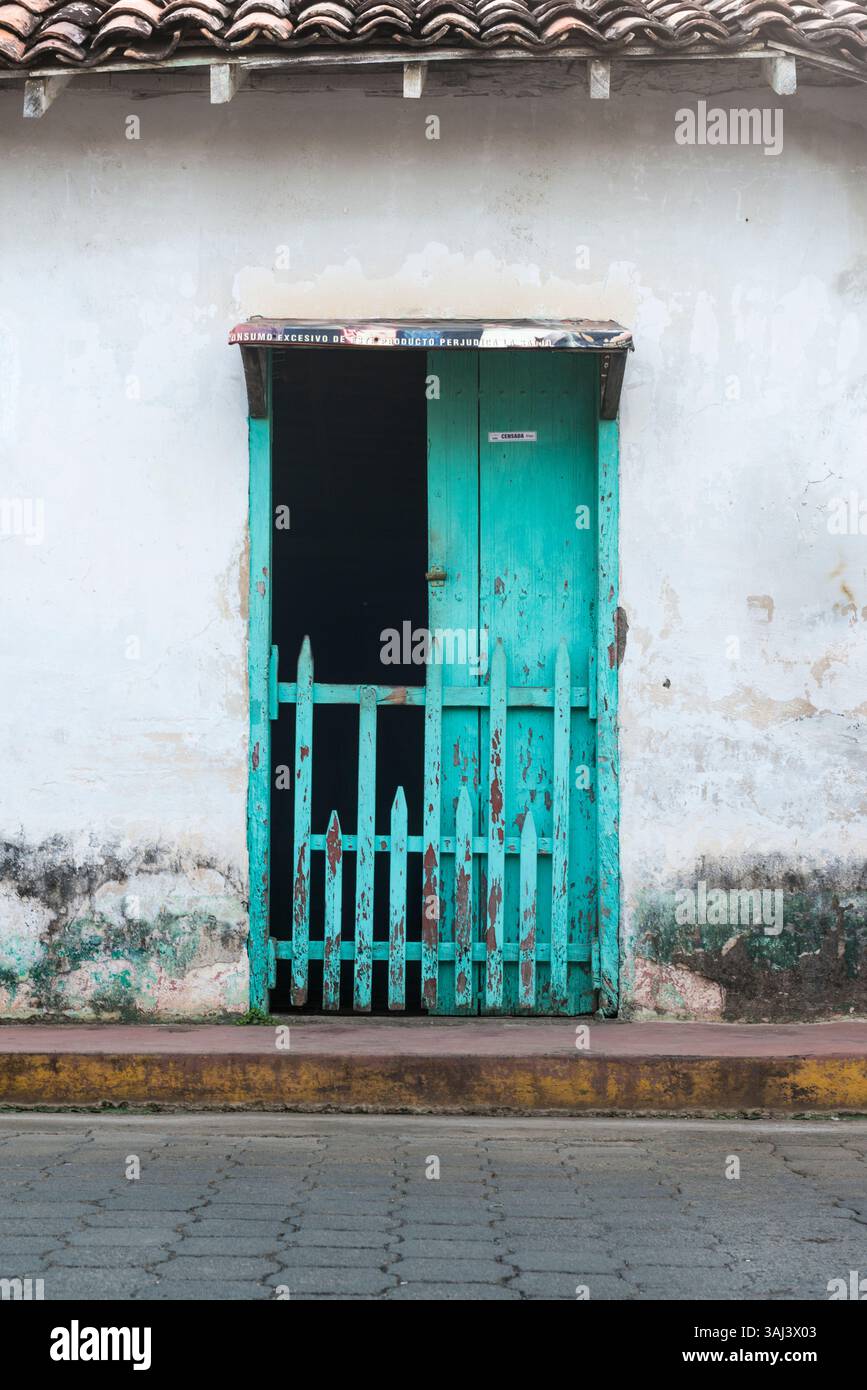 Unkempt porte en bois de couleur turquoise avec guichet dans le mur blanc moisi dans une rue au Nicaragua. Banque D'Images