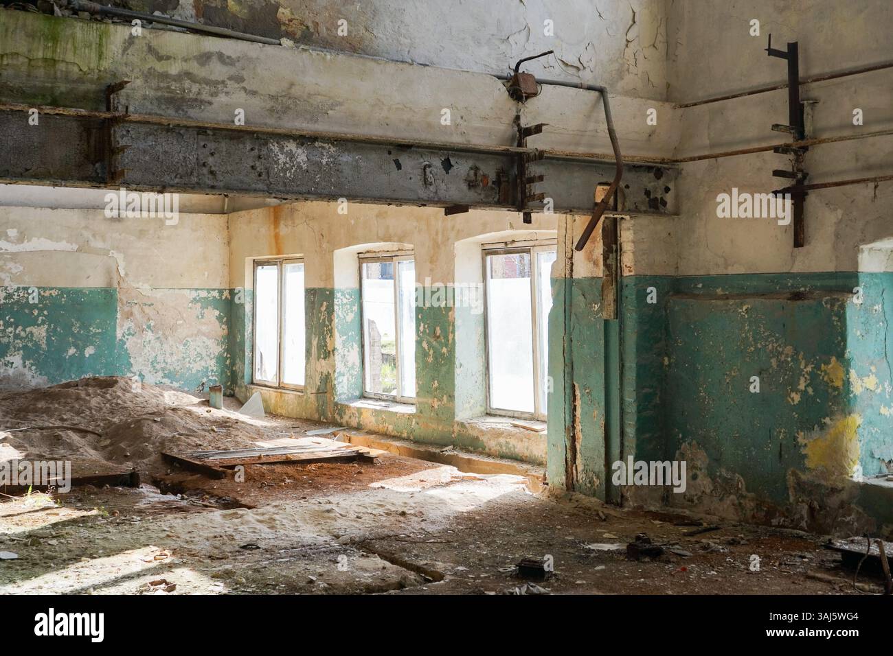 Une zone ensoleillée et couverte de sable dans une usine historique abandonnée, avec de grandes fenêtres cintrées. Idéal pour représenter la décadence urbaine, le patrimoine industriel. Banque D'Images