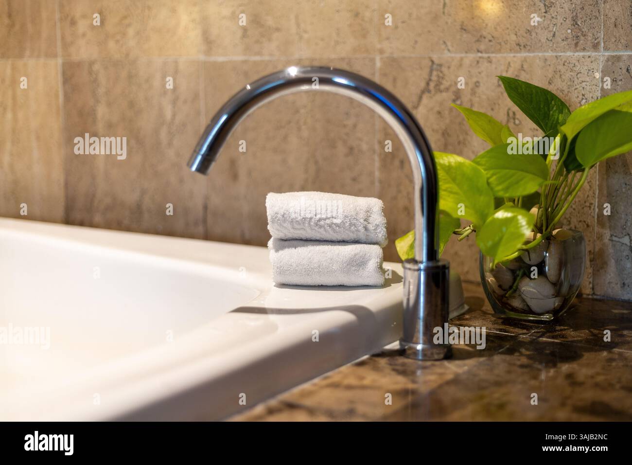 Dans une salle de bain confortable, un robinet moderne se trouve à côté de serviettes douces soigneusement empilées et une petite plante verte, créant une atmosphère paisible et accueillante pour re Banque D'Images