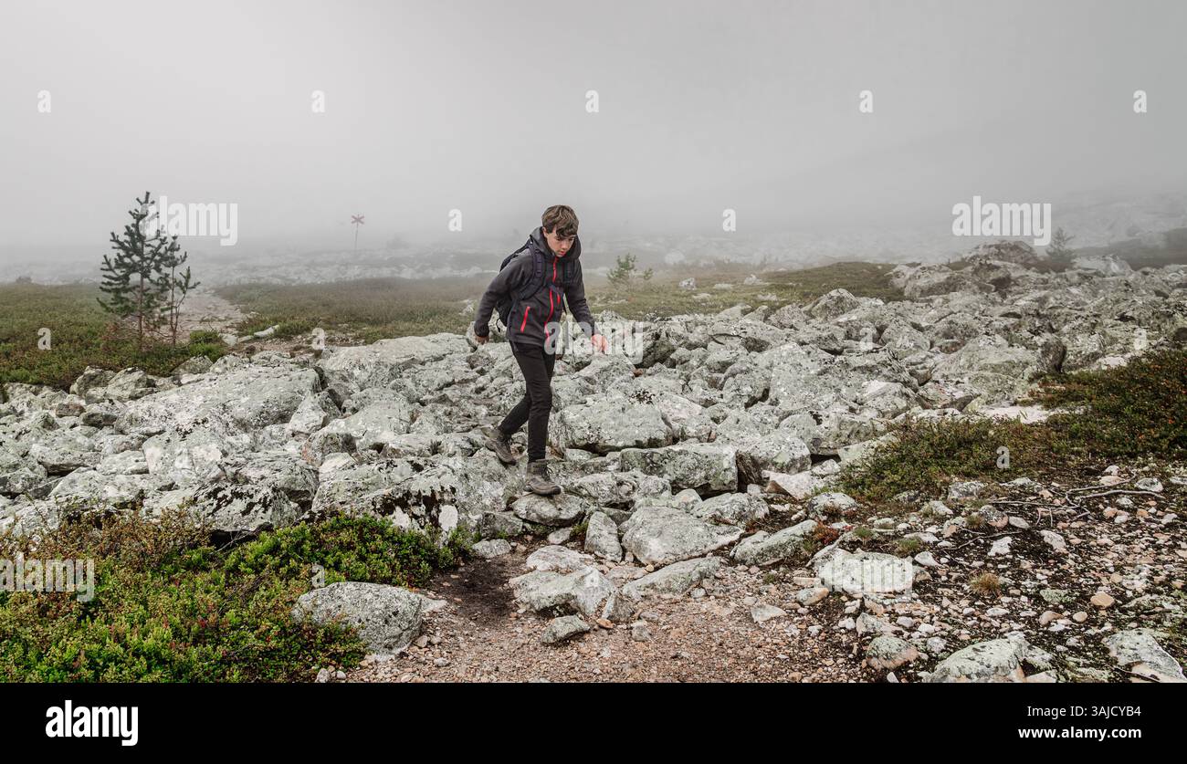 Garçon explorant le paysage accidenté de Dalarna, Suède, naviguant à travers un terrain rocheux dans la brume, profitant de la beauté de la nature tout en faisant de la randonnée Banque D'Images