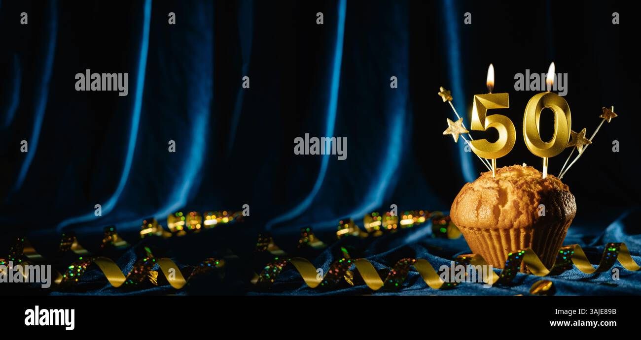 Numéro 50 bougie de célébration en or et petites étoiles dans un cupcake sucré sur fond de velours bleu vif. Concept de célébration d'anniversaire, anniversaire Banque D'Images