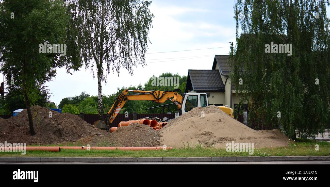 Excavatrice creusant du sable dans des pieux pour le changement de tuyaux. Chantier de construction pour travaux de changement de canalisations. Banque D'Images