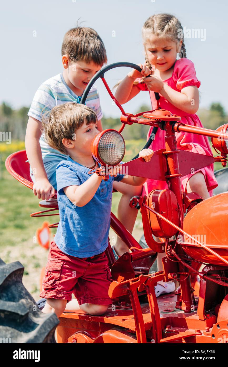 Trois enfants jouant sur un tracteur vintage rouge dans un champ ensoleillé Banque D'Images