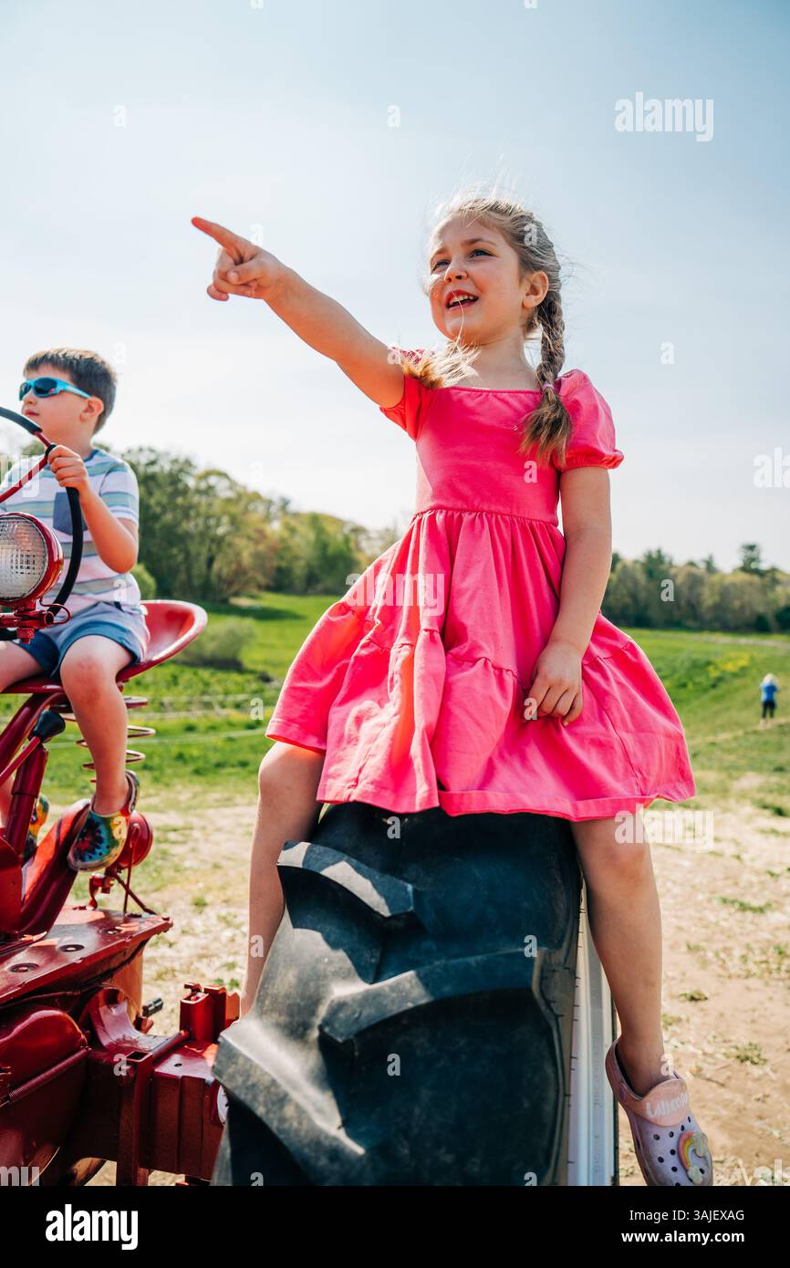 Fille pointant tout en étant assise sur le pneu du tracteur avec le garçon à proximité Banque D'Images